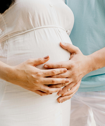 foto focana na barriga de uma grávida e seu parceiro, ambos com a mão na barriga. Foto por