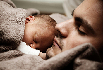 Foto com um homem e um recem nascido abraçados e aparentemente dormindo. Foto por Pixabay